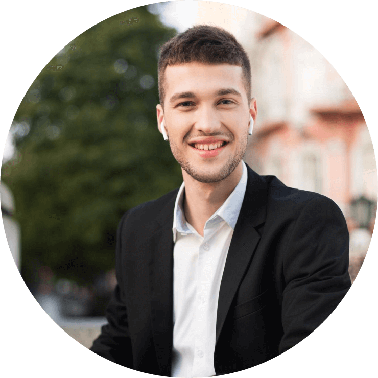 Youngcheerfulmaninclassicblacksuitandwhiteshirtwithwirelessearphoneshappilylookingincamerawithlaptopinhandswhilespendingtimeoutdoor2_a5nte_740