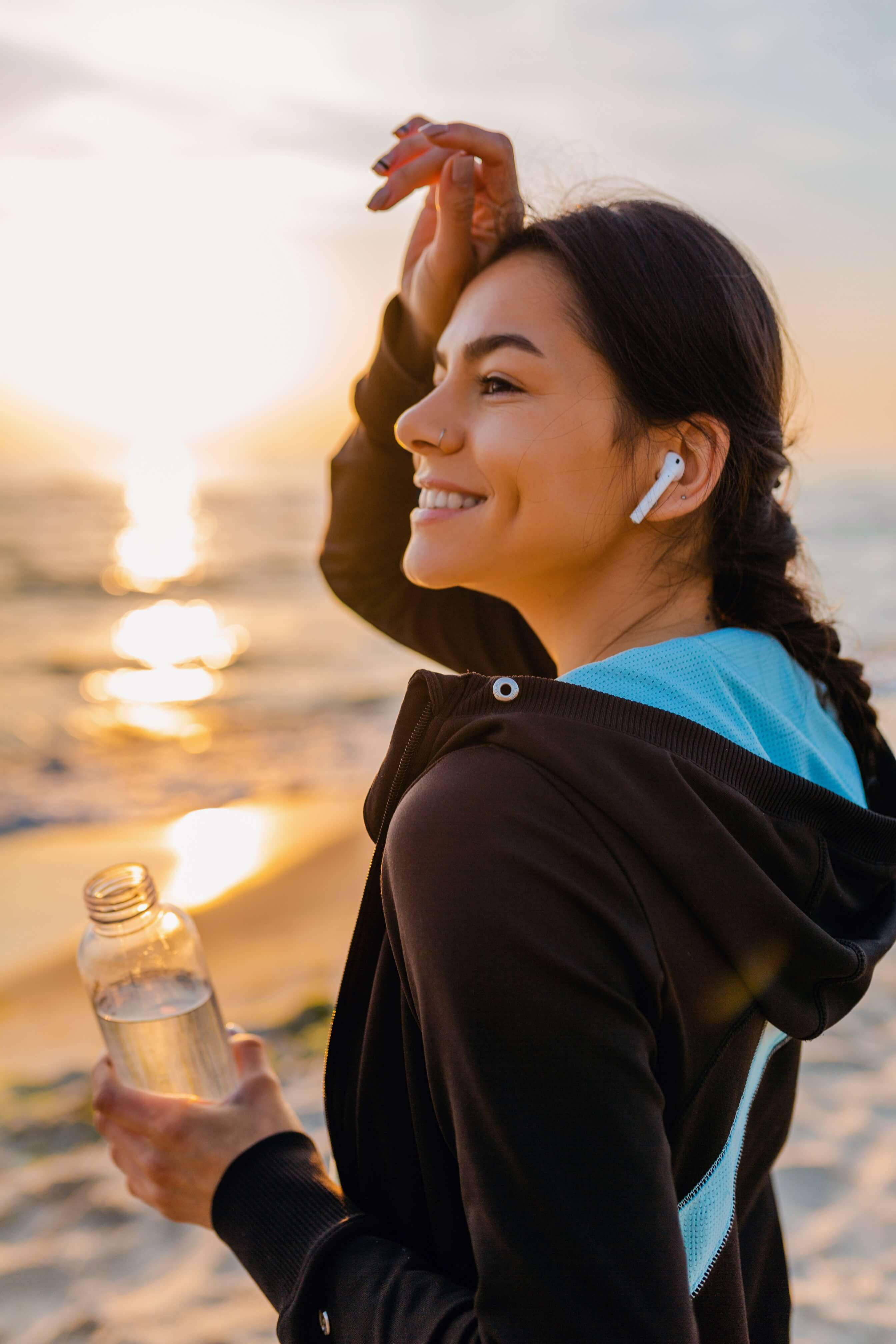 attractiveslimwomandoingsportexercisesmorningsunrisebeachsportswearthirstydrinkingwaterbottlehealthylifestylelisteningmusicwirelessearphoneshotsummerday1_m5nju_2688