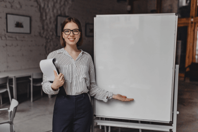 youngwomanblackwhiteoutfitglasseswithsmilelooksintocameraholdsdocumentspointswhiteofficeboard1_uzodq_390